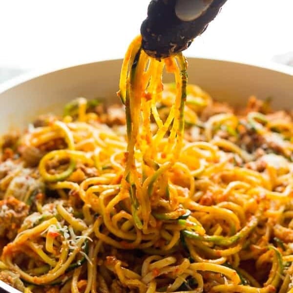 Tongs taking out ground turkey pasta in Romesco Sauce from white bowl