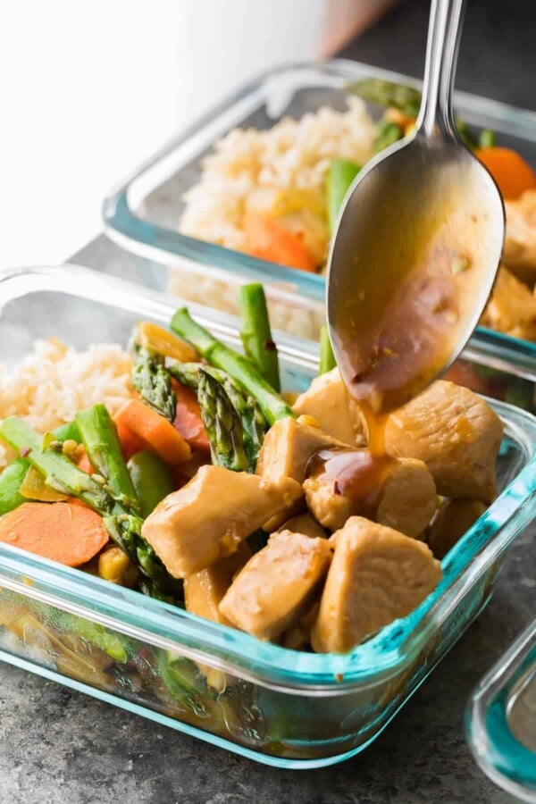 glass meal prep container with maple ginger chicken bowl and spoon drizzling the dressing