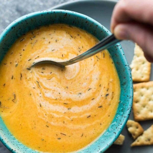 Overhead shot of carrot ginger soup in a blue bowl with a spoon stirring it