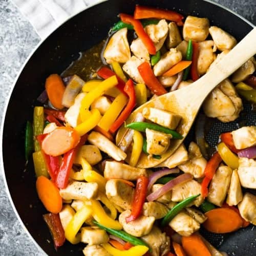 overhead shot of honey sriracha chicken stir fry in skillet with wood spoon