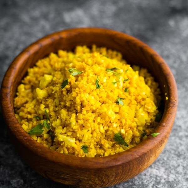golden turmeric cauliflower rice in wood bowl on gray background