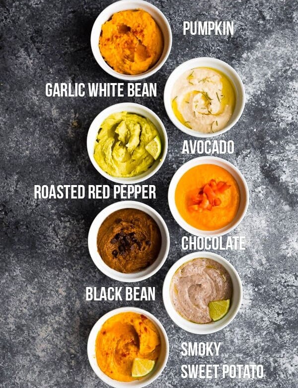 overhead shot of 7 different hummus recipes in white bowls with labels