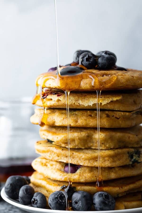 side image of stack of blueberry pancakes with syrup and fresh blueberries