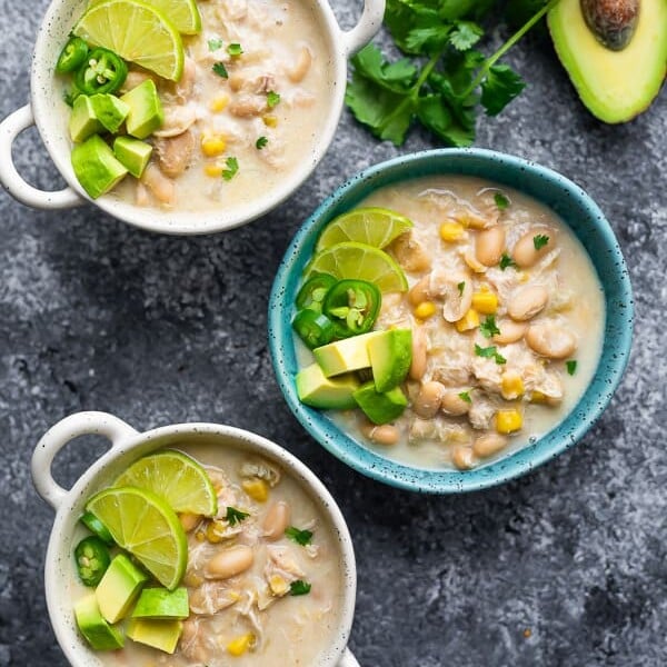 overhead shot of three bowls filled with white chicken chili with cilantro and half avocado next to bowls