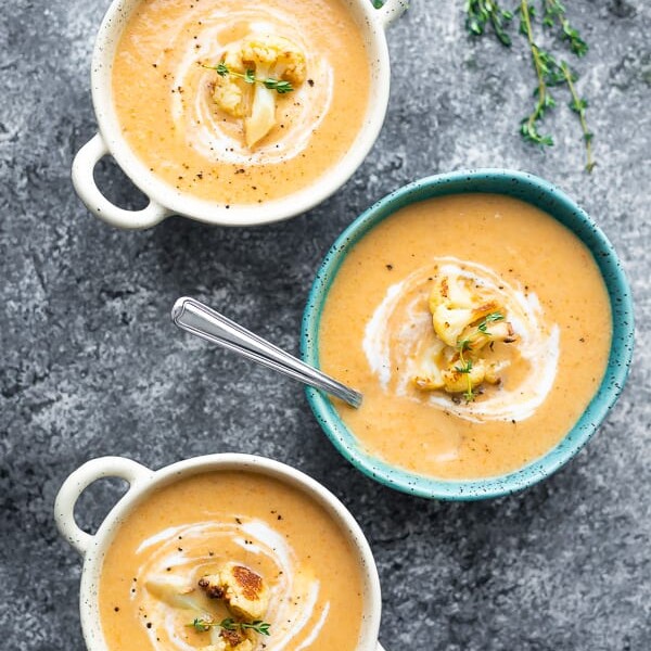 overhead shot of three bowls filled with creamy roasted cauliflower soup on a gray background