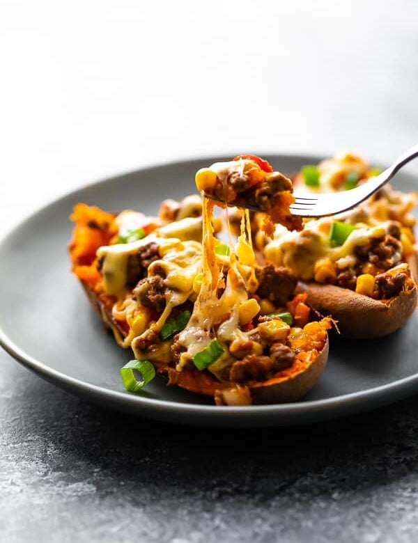 Two taco stuffed sweet potatoes on a gray plate with fork taking a bite